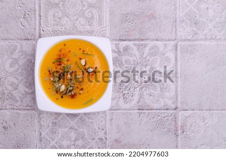 Yellow thick soup with nuts, seeds and red pepper on a light background. Top view.