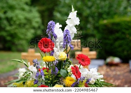 colorful flowers as grave arrangement after a funeral in front of wooden crosses in blurred background Royalty-Free Stock Photo #2204985467
