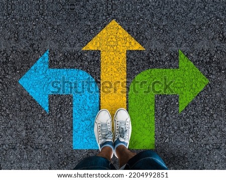  man legs in sneakers standing on road with three direction arrow choices, left, right or move forward  Royalty-Free Stock Photo #2204992851