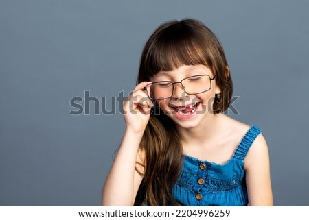 A funny positive little girl put on adult glasses on her face and laughs merrily and smiles with fallen milk teeth. Ophthalmologist and vision care. Emotional photo, happy preschool child.