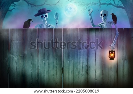 Happy Halloween holiday background.  Funny skeletons peeking over a wooden fence.  Halloween card with copy space.
