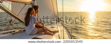 Panorama of young Hispanic couple at leisure sailing the ocean relaxing on luxury yacht watching the sunset on the horizon Royalty-Free Stock Photo #2205013545