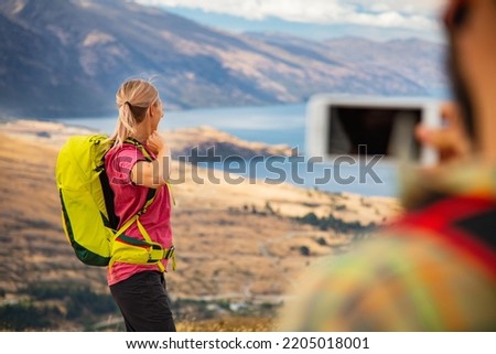 New Zealand successful young Caucasian couple taking travel pictures near Lake Wakatipu Queenstown while on trekking adventure holiday outdoors The Remarkables Otago