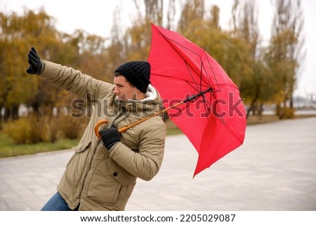 Man with red umbrella caught in gust of wind outdoors
