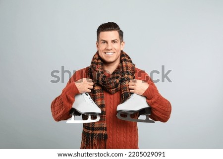 Happy man with ice skates on grey background