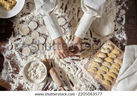 The process of making dumplings. The woman is dressed in a white, traditional Ukrainian vyshyvanka and a brown skirt. She makes dumplings on the table with her hands. Wraps mashed potatoes in round do