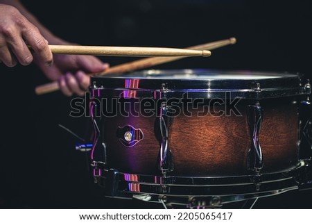 Drummer playing drum sticks on a snare drum on black background.