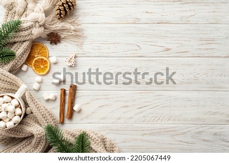 Winter mood concept. Top view photo of pine cone spruce branches cup of cocoa with marshmallow knitted plaid dried orange slices anise cinnamon sticks on white wooden desk background with copyspace