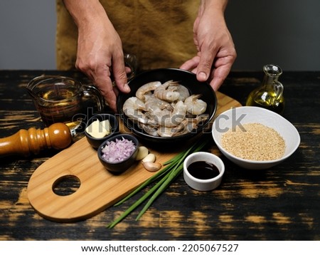Cher hands cooking recipe with big tiger shrimps, rice, sauce and other ingredients on table background 