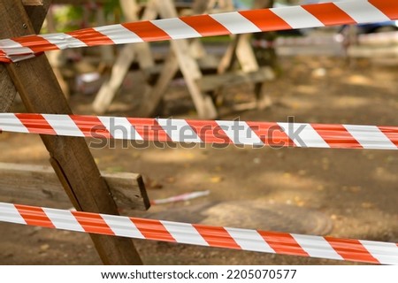 Red and white warning tape stretched across a blurred background with ground. Protection tape defining the border of a dangerous zone of construction work in process.