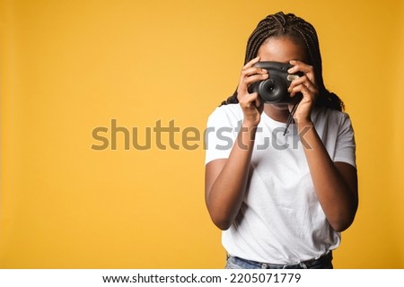 African-american woman taking photo of you. Female holding polaroid camera and pushing button standing isolated on yellow, making instant photo with retro camera