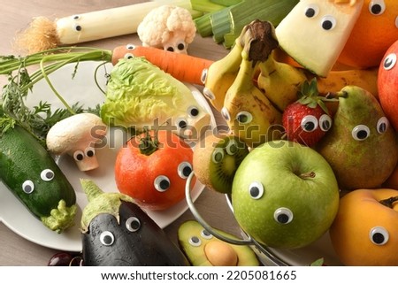 Child nutrition concept with fruits and vegetables with eyes in containers on wooden table. Top elevated view. Royalty-Free Stock Photo #2205081665