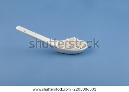 White chemical powder in ceramic spoon on blue. Food coloring, E171. Titanium dioxide, TiO2. Pigment present in of paint, food, toothpastes,  chewing gum, pills, tablets and cosmetic products. Royalty-Free Stock Photo #2205086301