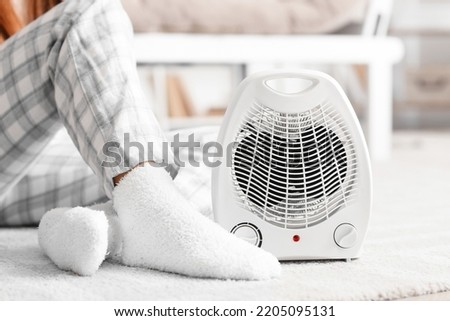 Electric fan heater and woman in warm socks on floor at home, closeup Royalty-Free Stock Photo #2205095131