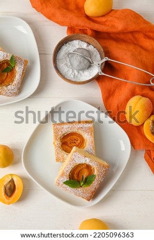 Plates with pieces of tasty apricot pie and sugar powder on light wooden background Royalty-Free Stock Photo #2205096363