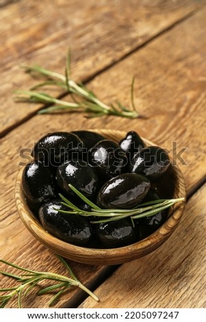 Bowl of tasty black olives on wooden background