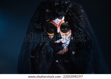 woman in sugar skull halloween makeup gesturing near black veil on dark blue background