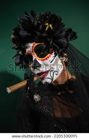 Portrait of woman in santa muerte halloween costume holding cigar on green background