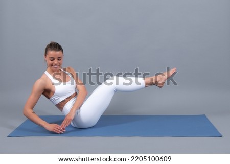 Six pack abs training. Young sporty woman in sportswear practicing fitness on mat, beautiful girl doing exercise, working out on gray studio background.