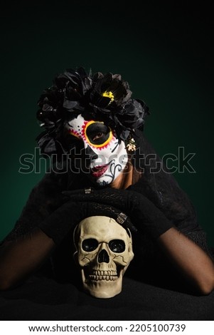Woman in mexican halloween costume touching skull on dark green background