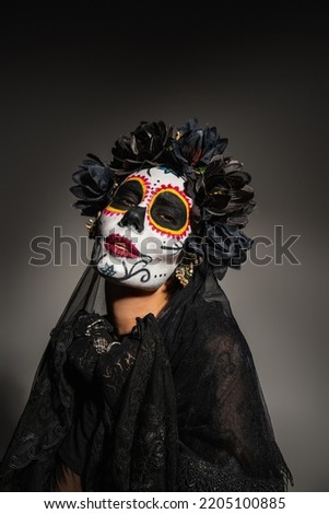 Portrait of woman in mexican day of dead costume looking at camera on black background