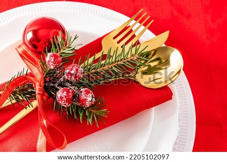 the near view of part of the plates serving the New Year's table. gold cutlery with a spruce branch and red balls on a red background