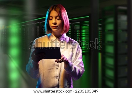 Hosting provider employee. Woman in data center. Girl with tablet computer. Woman indoors hosting company. Career in hosting business. Woman manager near green server rack. Telecommunication business