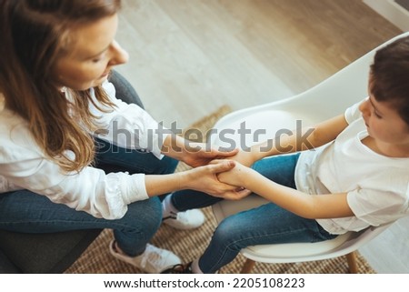 Young female school psychologist having serious conversation with smart little boy at office. Close up image mother and son palms, mommy holding hands of kid.  Concept of counsellor