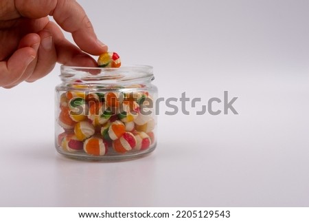 Hand takes colorful candy from glass jar, on isolated white background, colorful unhealthy candies close up, place to copy