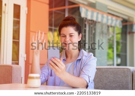 Smiling millennial woman outside with smartphone,waved her hand.Providing video call or online conference.