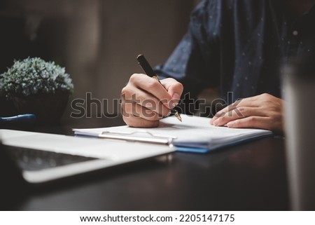 Hand holding pen writing paperwork business document financial investment or signature contract job and insurance on desk.