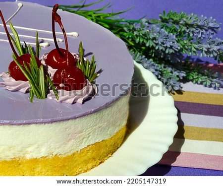 Mousse dessert decorated with cherries and rosemary sprigs on a white plate on a purple background. Delicious birthday cake.