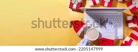 Christmas sale, preparation for holidays concept. Santa Claus hands with laptop, hot chocolate latte cup, gift boxes, flat lay on golden background. Making wishlist, preparation gifts for Christmas.