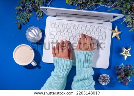 Christmas sale, preparation for holidays concept. Winter office workplace background. Laptop, hot chocolate latte cup with Christmas toys, winter tree branches, flat lay on bright blue background