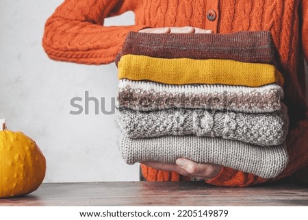 A woman holding a stack autumn warm knitted sweaters. Change of season and wardrobe. autumn slow fashion concept Royalty-Free Stock Photo #2205149879