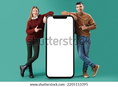 Happy young couple and big smartphone on green background