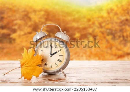Alarm clock and autumn leaf on table outdoors. Daylight saving time end Royalty-Free Stock Photo #2205153487