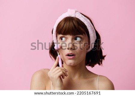 horizontal beauty photo of a funny, surprised woman with short hair holding a roller for massage, leaning it against her cheek and looking at the camera with her mouth wide open