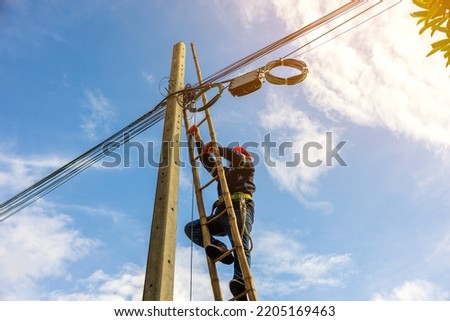 A telecoms worker is shown working from a utility pole ladder while wearing high visibility personal safety clothing, PPE, and a hard hat.	 Royalty-Free Stock Photo #2205169463