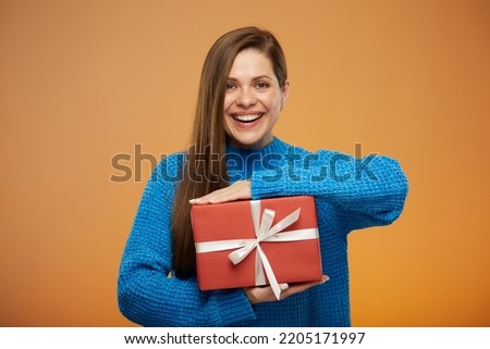 Smiling woman in blue warm sweater holding gift box. Isolated female portrait on orange.
