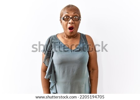 Mature hispanic woman wearing glasses standing over isolated background afraid and shocked with surprise and amazed expression, fear and excited face. 