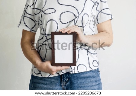 A woman in a white T -shirt and jeans holds a empty dark wooden frame with place for text in her hands. photo for advertising text