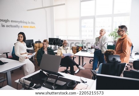 Group of businesspeople of different age brainstorming business startup and analyzing documents while working in modern workshop with gadgets together. Colleagues having meeting in office Royalty-Free Stock Photo #2205215573