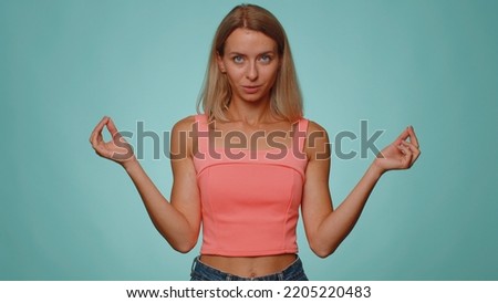 Keep calm down, relax, inner balance. Woman breathes deeply with mudra gesture, eyes closed, meditating with concentrated thoughts, peaceful mind. Young girl isolated on blue studio wall background