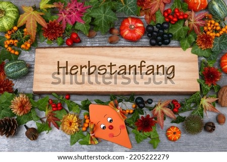 The lettering  Herbstanfang written on a board with autumnal decorations. Herbstanfang means the beginning of autumn.