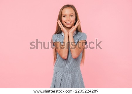 Emotional young smart caucasian preteen teenage girl schoolgirl looking at camera with toothy smile isolated in pink background