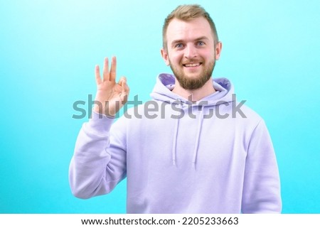 Man in a purple who is showing OK gesture on his hand on a blue background￼. Gesturing. Handsome. Happiness. Smart. Professional. Job. Alright. Positively. Fine. Well. Perfect. Fair. Exactly. Correct Royalty-Free Stock Photo #2205233663
