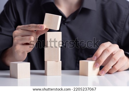 Man's hand completing set of 4 stacked wooden cubes, man build a tower by using four blank wooden cube on table. Mockup for letters, symbol, picture text, word, idea and concept.