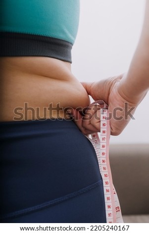 Beautiful fat woman with tape measure She uses her hand to squeeze the excess fat that is isolated on a white background. She wants to lose weight, the concept of surgery and break down fat under the Royalty-Free Stock Photo #2205240167