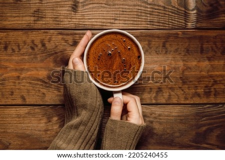 Hands hold cup of coffee close up on wooden dark background, top view, flat lay